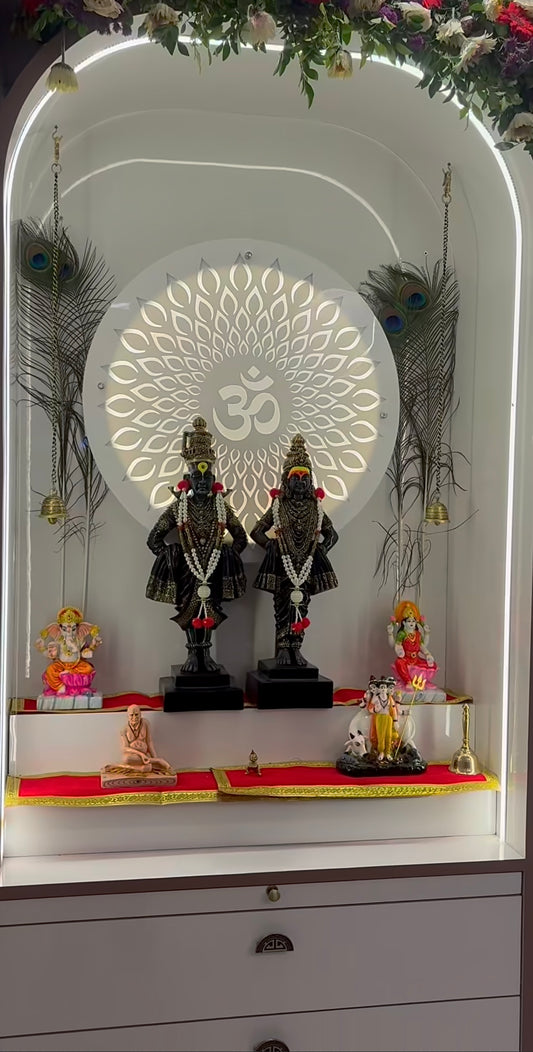 Luxury white Pooja mandir with LED backlit Om symbol, floral arch decoration, and storage drawers, showcasing black Vitthal-Rukmini idols with garlands.
