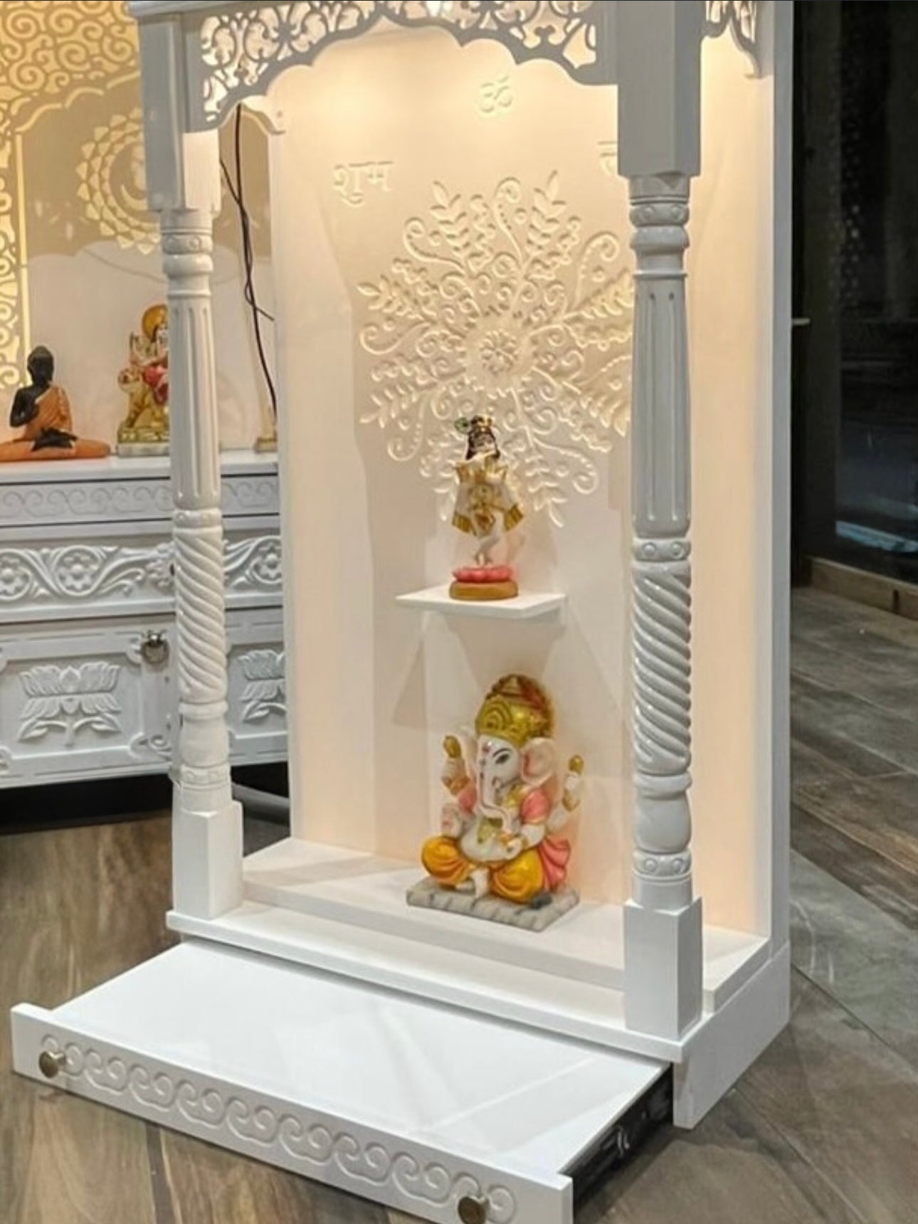 Modern white wooden pooja mandir with LED Corian back panel, drawer, and intricate carving for home temple decor.