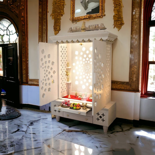 Luxury white wooden pooja mandir with intricate cut-out patterns, golden accents, and warm backlighting, placed in a grand marble-floored interior.