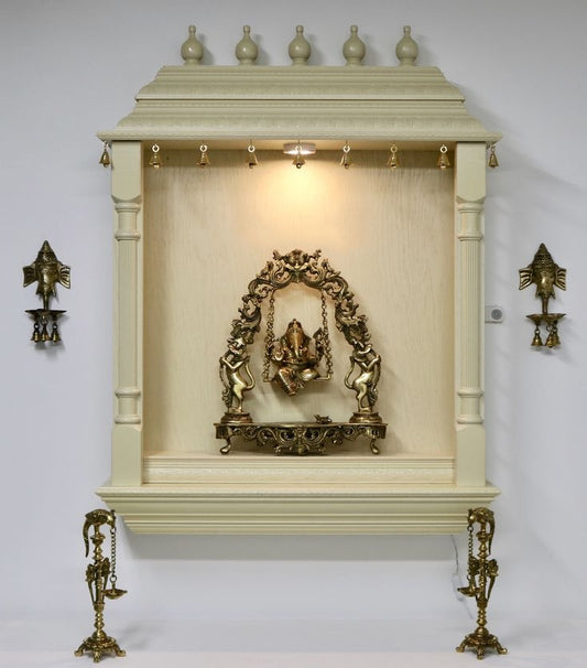 Wall-mounted wooden temple with brass Ganesha idol on a swing, ornate arch frame, and traditional hanging bells, ideal for home mandir decoration.