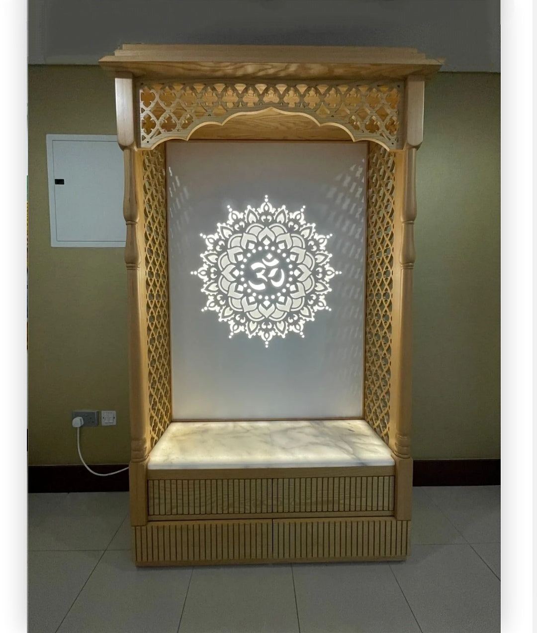 Traditional wooden Pooja temple featuring decorative lattice panels and glowing Om symbol, enhancing spiritual ambiance.