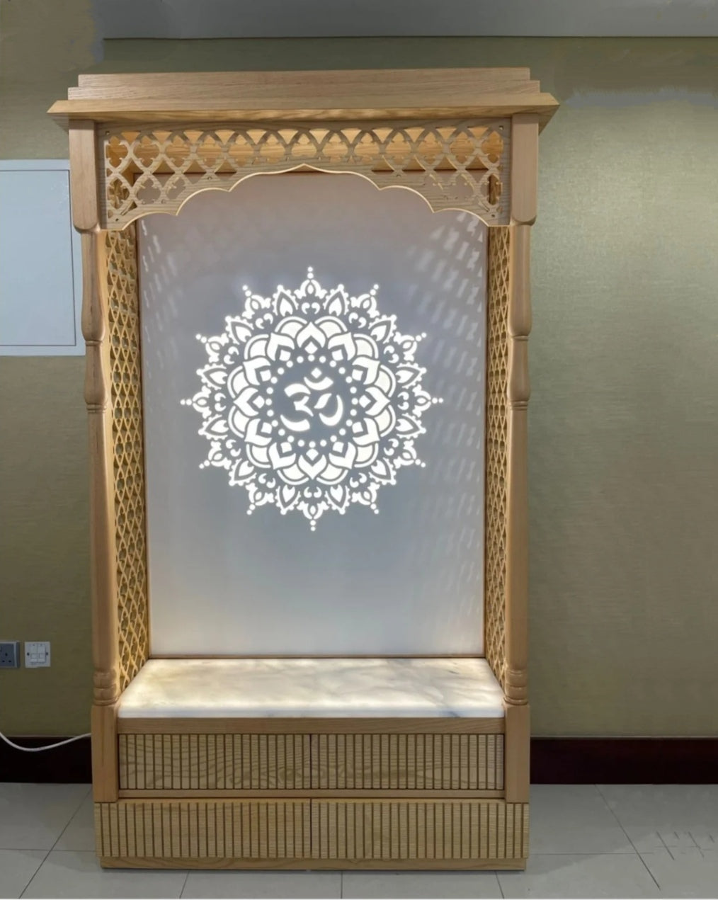 Elegant wooden Pooja temple with intricate lattice design and illuminated Om mandala backdrop, perfect for home prayer space.